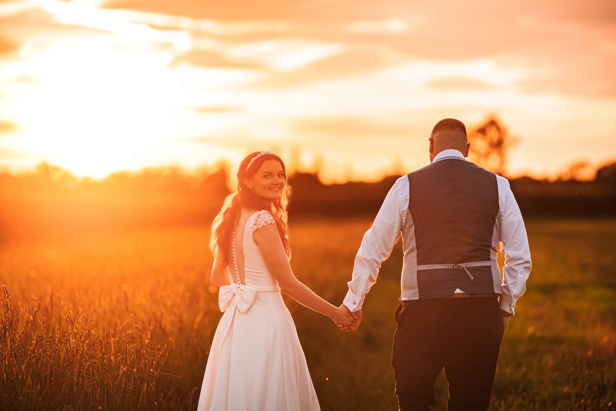 Sarah looks back at the camera as she and Phil walk through a sunlit field at Woolas Barn.