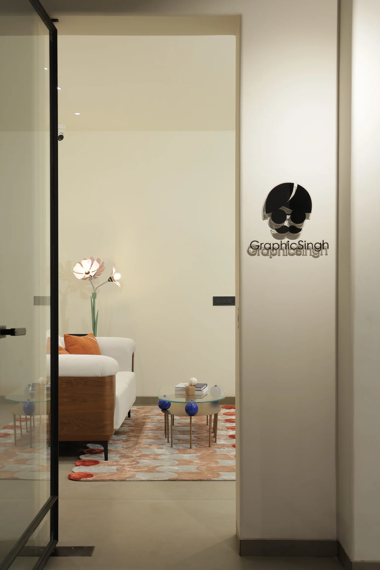 Modern office lobby with a glass door entrance, featuring a cozy white sofa, colorful cushions, a stylish coffee table, and a decorative floor lamp against a light interior, emphasizing a welcoming and contemporary design.