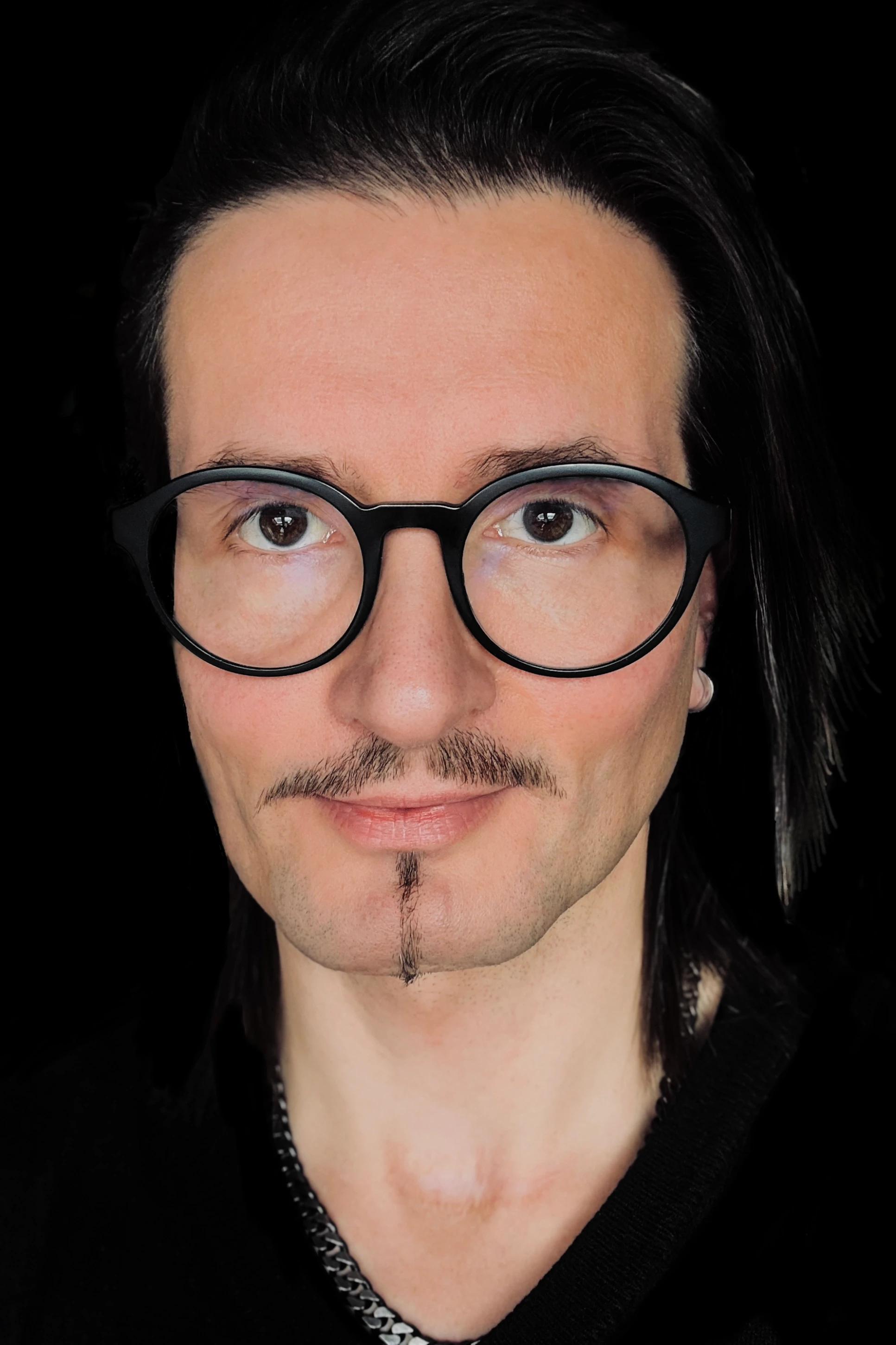 Porträt von Jens Pfeifer vor schwarzem Hintergrund, mit runder schwarzer Brille und schmalem Schnurrbart, direkter Blick in die Kamera.