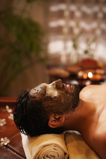 Ayurvedic beauty care treatment – A man receiving a herbal facial therapy at a wellness resort, surrounded by a relaxing spa ambiance with candles and flowers