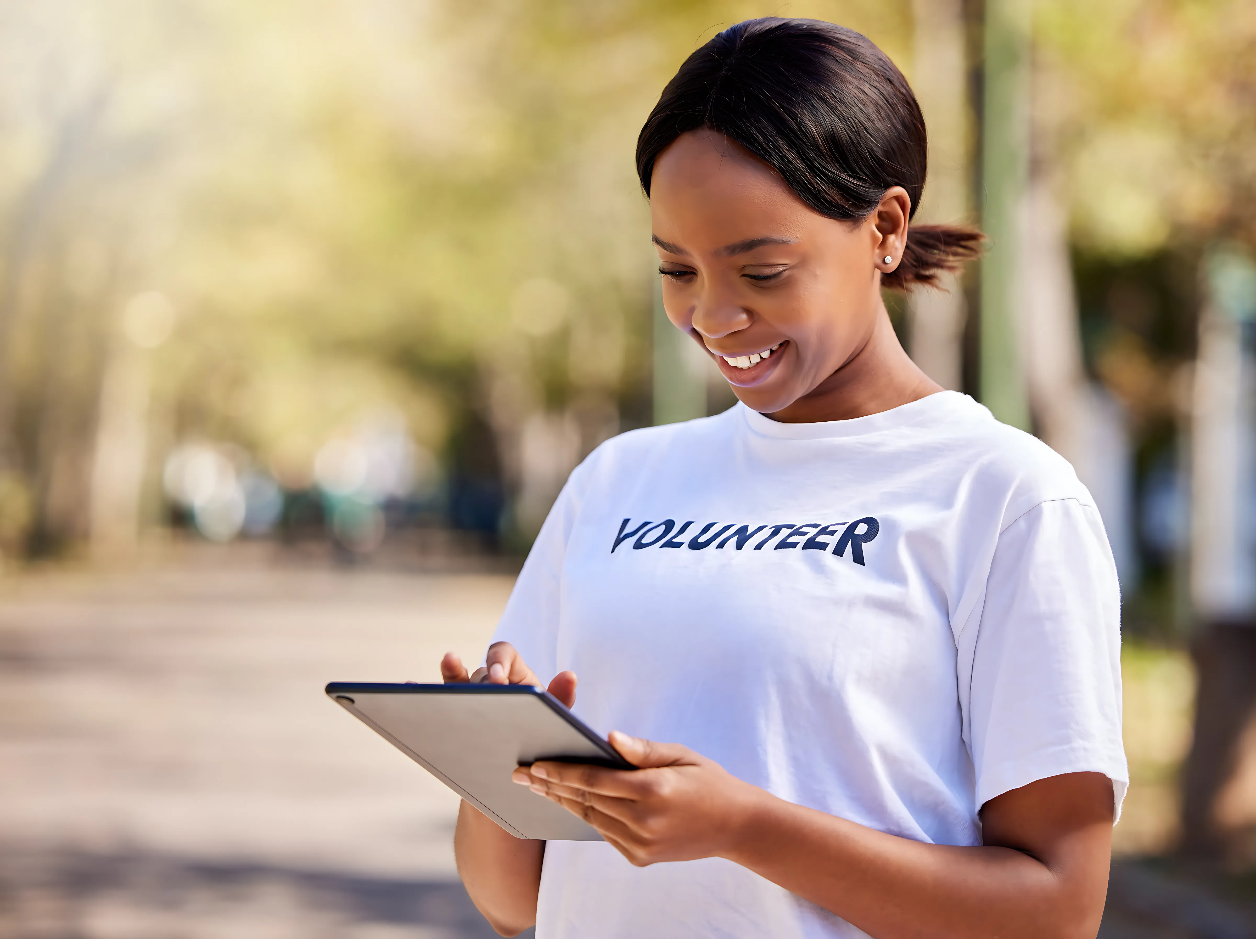 A young person with curly hair smiles at the camera while sitting in front of a laptop against a dark background.
