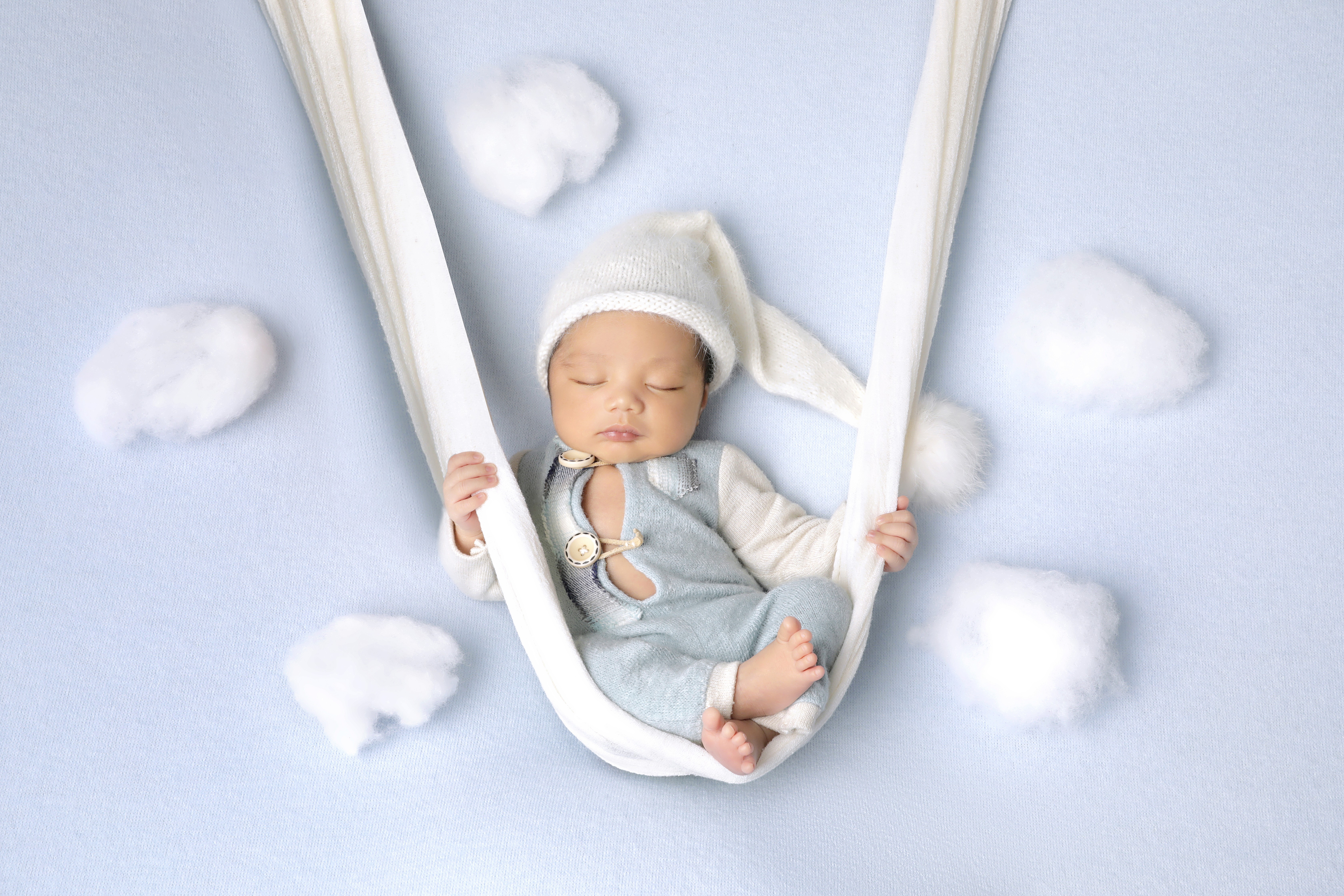 Infant sleeping and sitting snugly on a cloth swing as a baby photography prop.