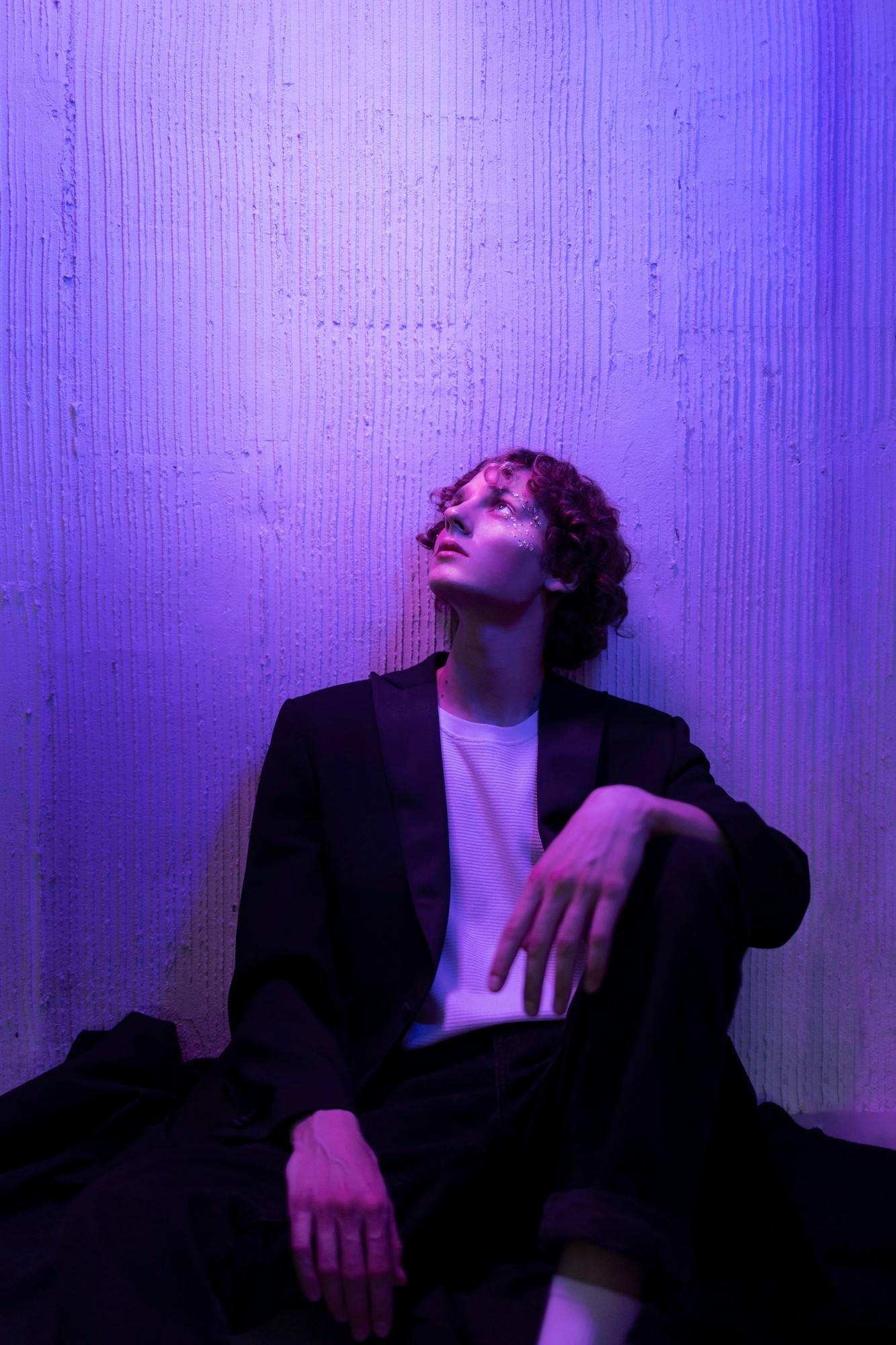 Low-angle black and white shot of a man in a blazer looking upwards, featuring dramatic shadows and grainy film texture.