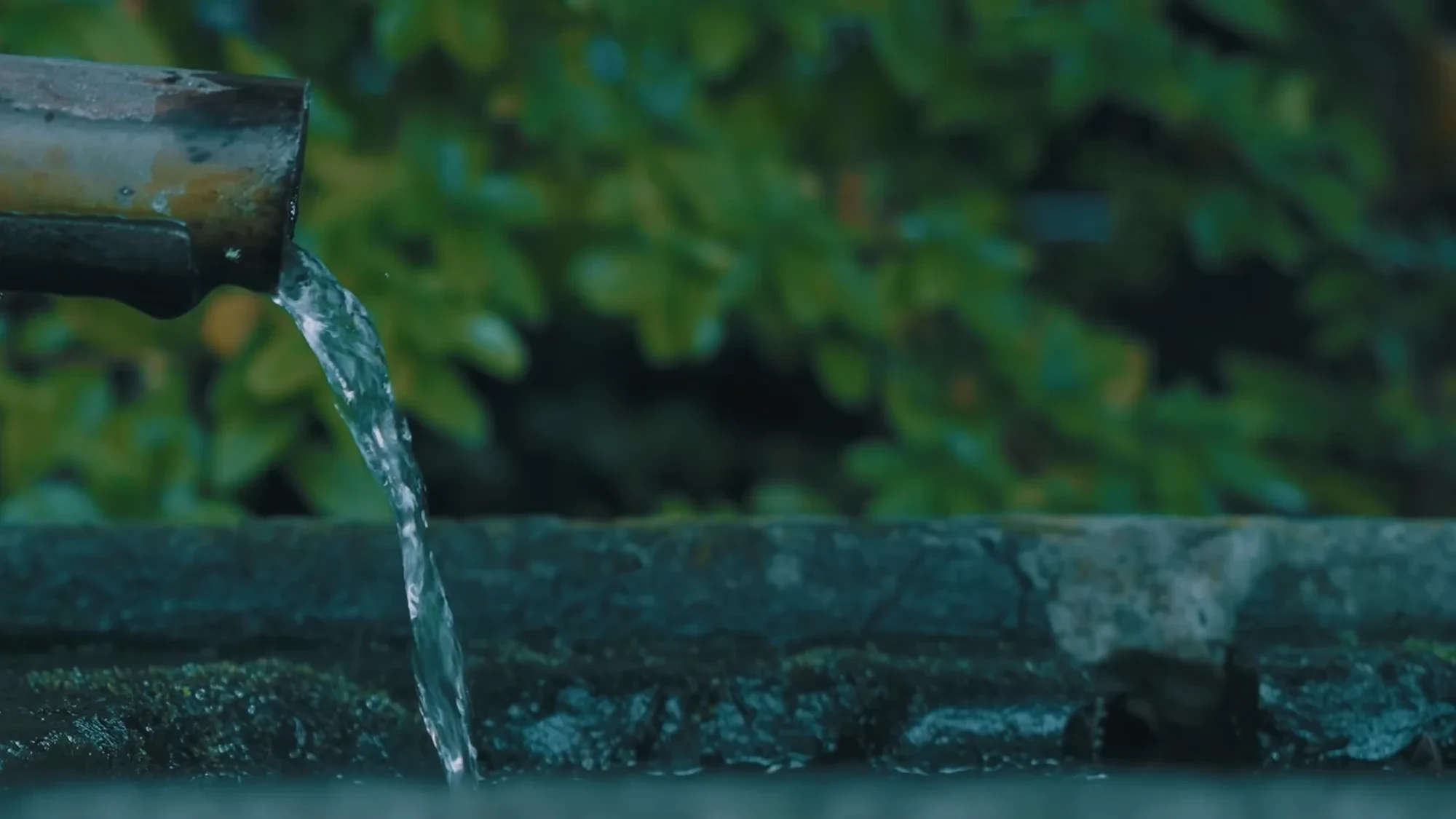 Hot spring water pouring from a bamboo spout onto a stone lip at Kurokawa Onsen