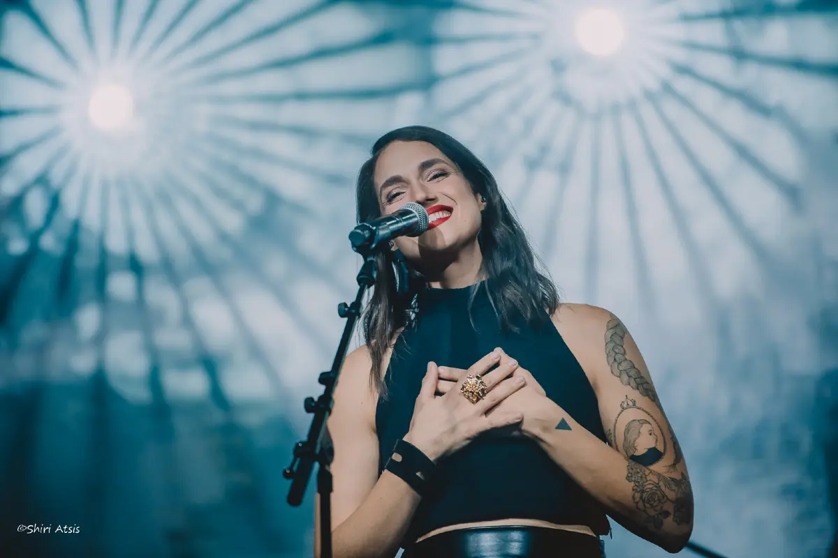 פורטרט של מארינה מקסימיליאן מחייכת על הבמה עם יד על הלב, צילום הופעות אומנותי מאת שירי עציץ - Shiriz.