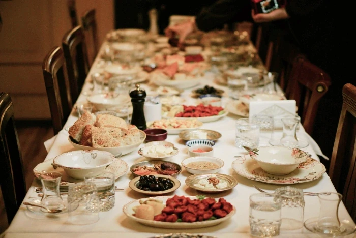 A long dinner table in warm light generously dressed with various family-style dishes and glassware. 