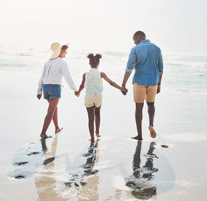 mom and dad holding daughter's hand on beach