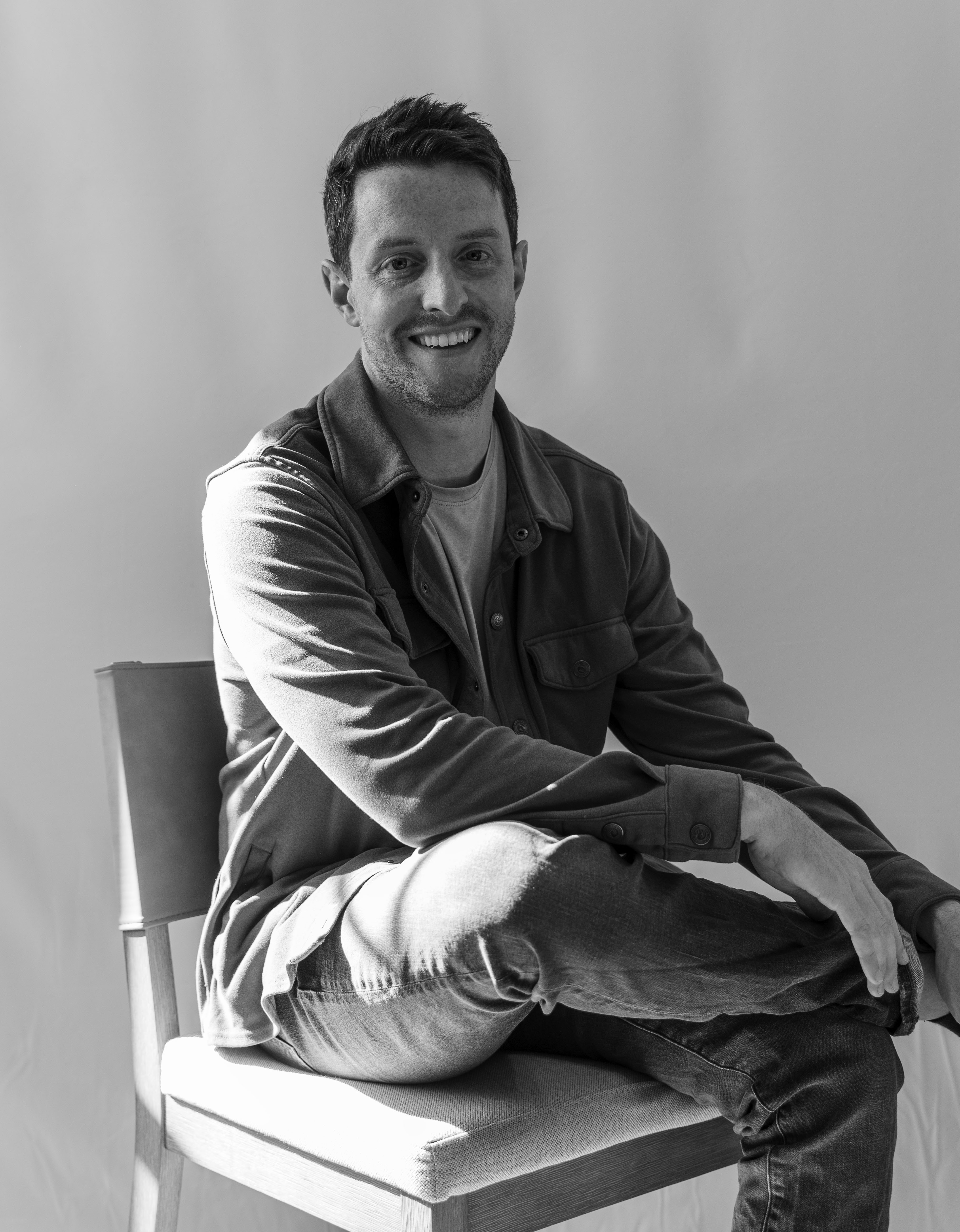 photo headshot of a man in a buttoned shirt sitting in a chair