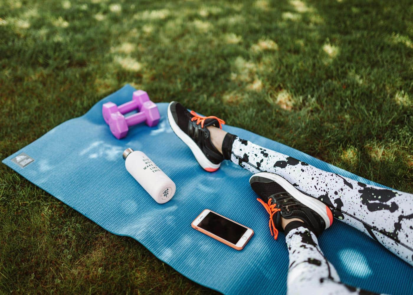 Person with black an white leggings sitting on blue yoga mat with small weights, water container, and iPhone