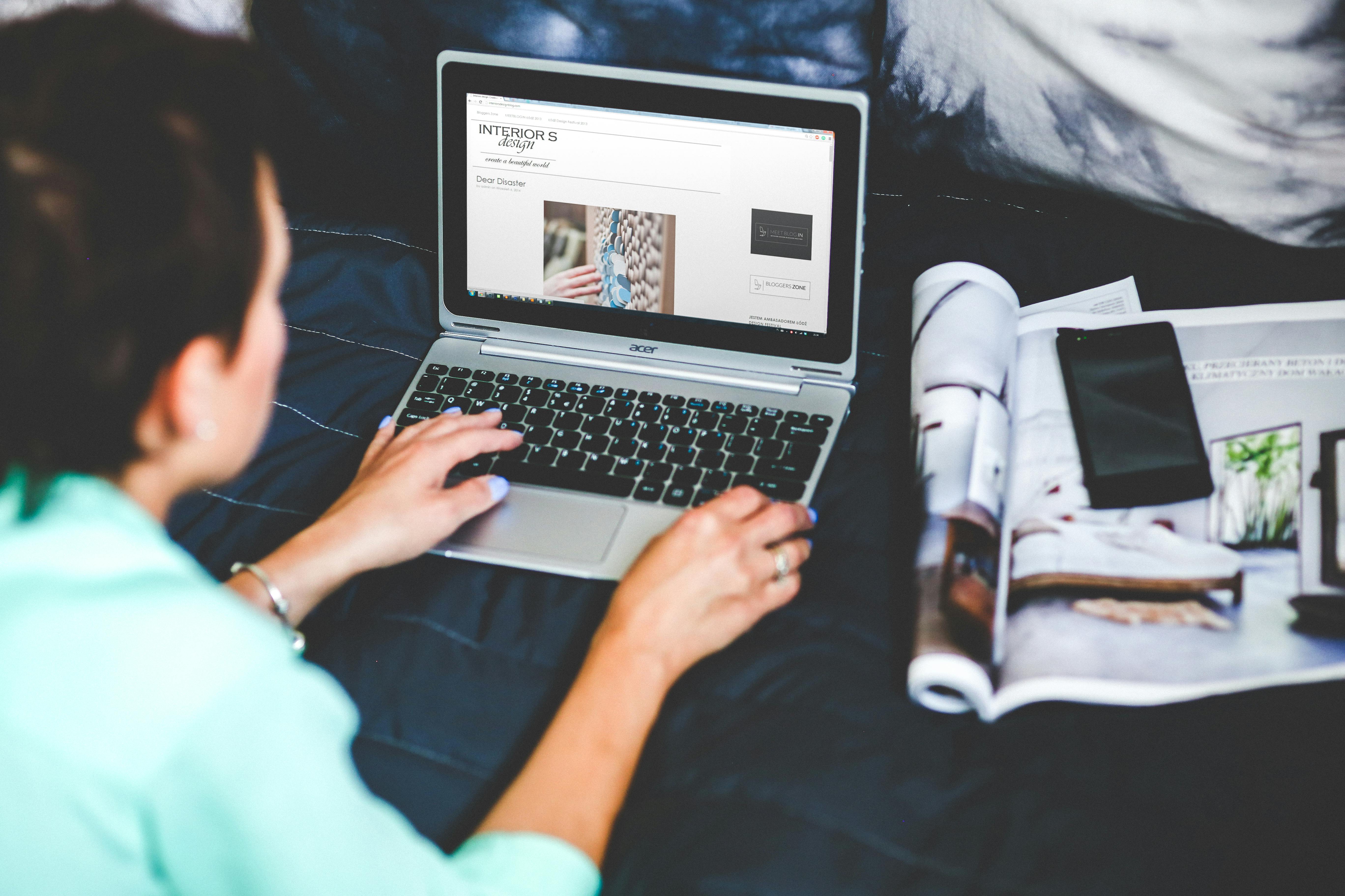 Woman with laptop lying down in bed reading an online newsletter