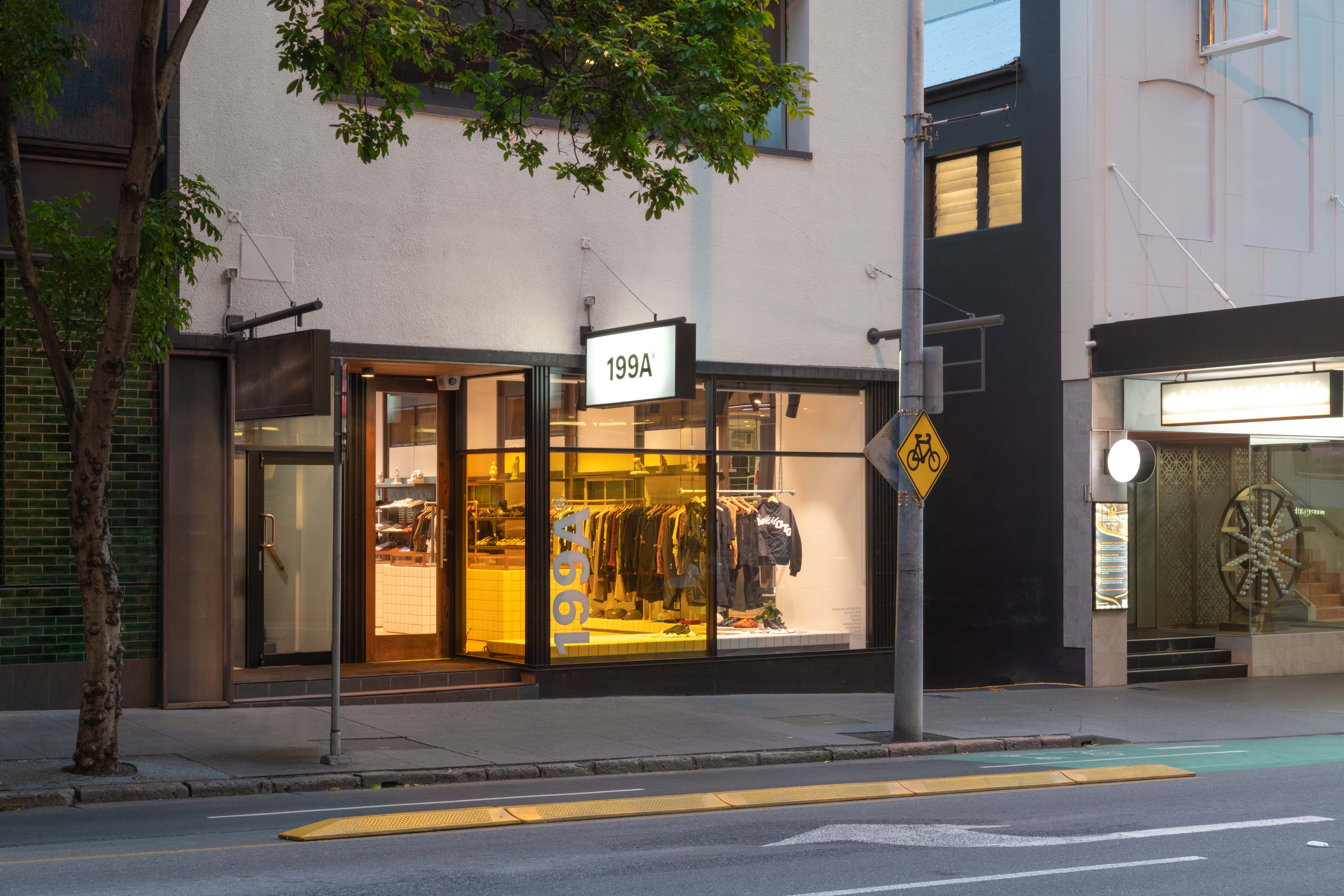 Exterior views of the 199A® storefront at dusk, showing the warmly lit interior through large windows, bold signage, and the store’s presence within the surrounding urban streetscape.