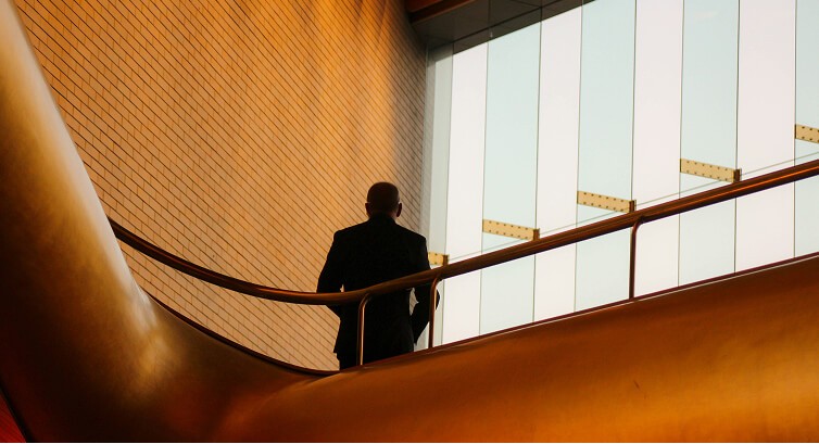 Business professional in silhouette walking up modern wooden stairs in a contemporary office building with large windows and warm lighting