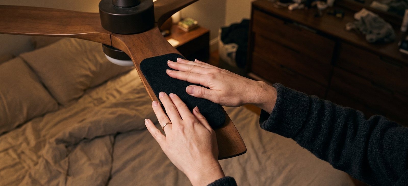 Pressing a matte black Barnakl pad onto the top of a ceiling fan blade.