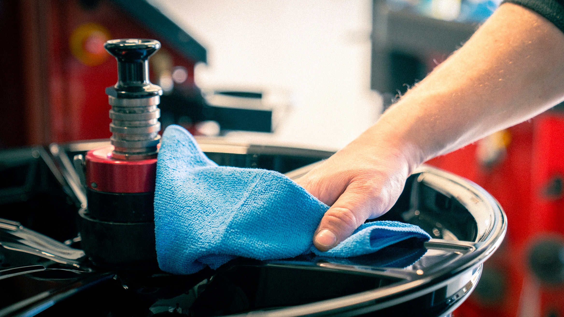 Schwarz-weiß Aufnahme einer Hand, die mit einem Tuch eine glänzende Felge poliert – ein Moment der Sorgfalt und Qualität in der Felgenaufbereitung.