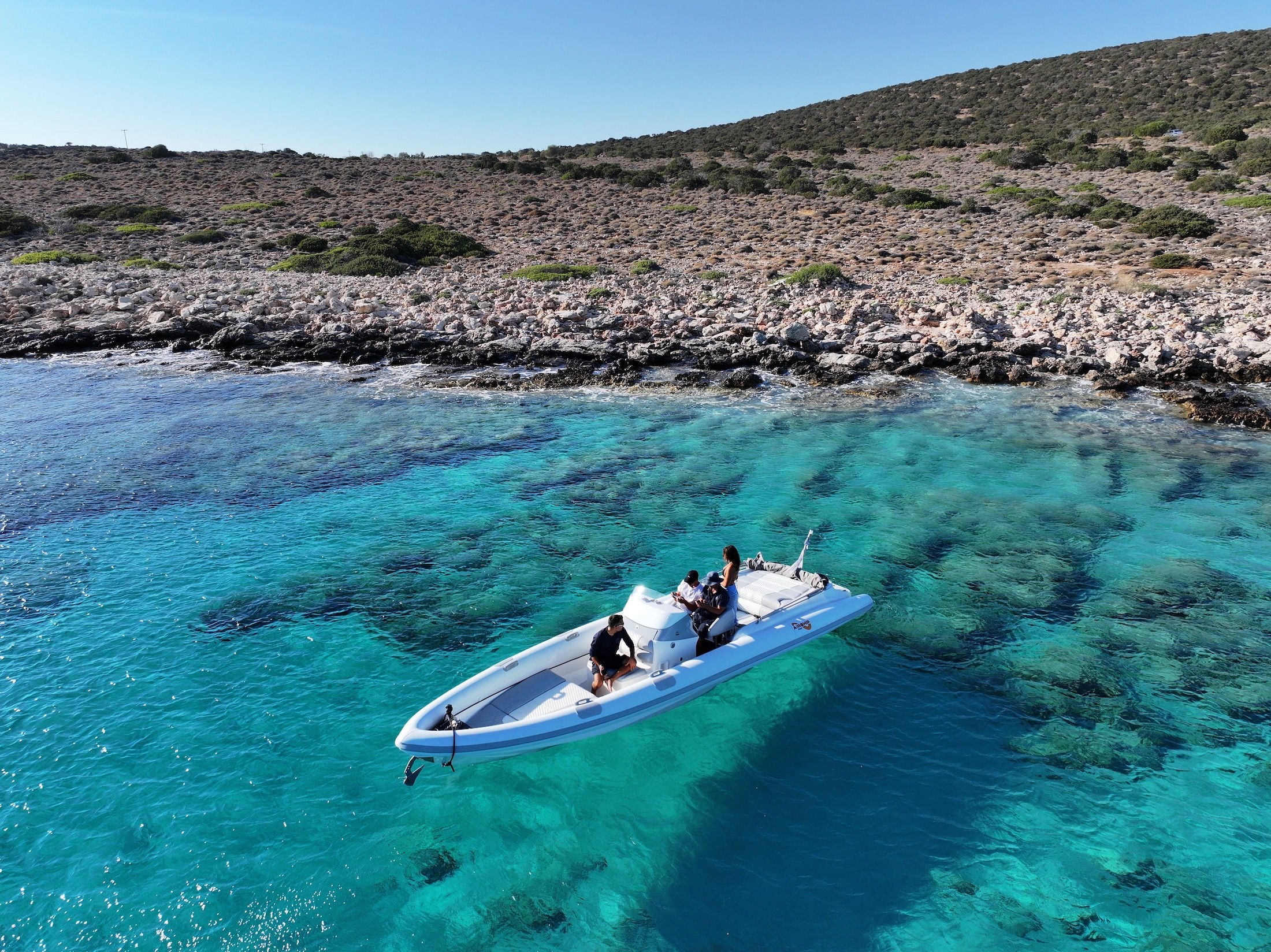 White Airship 30 yacht cruising through crystal-clear blue waters along dramatic limestone cliffs in the Cyclades under clear skies.