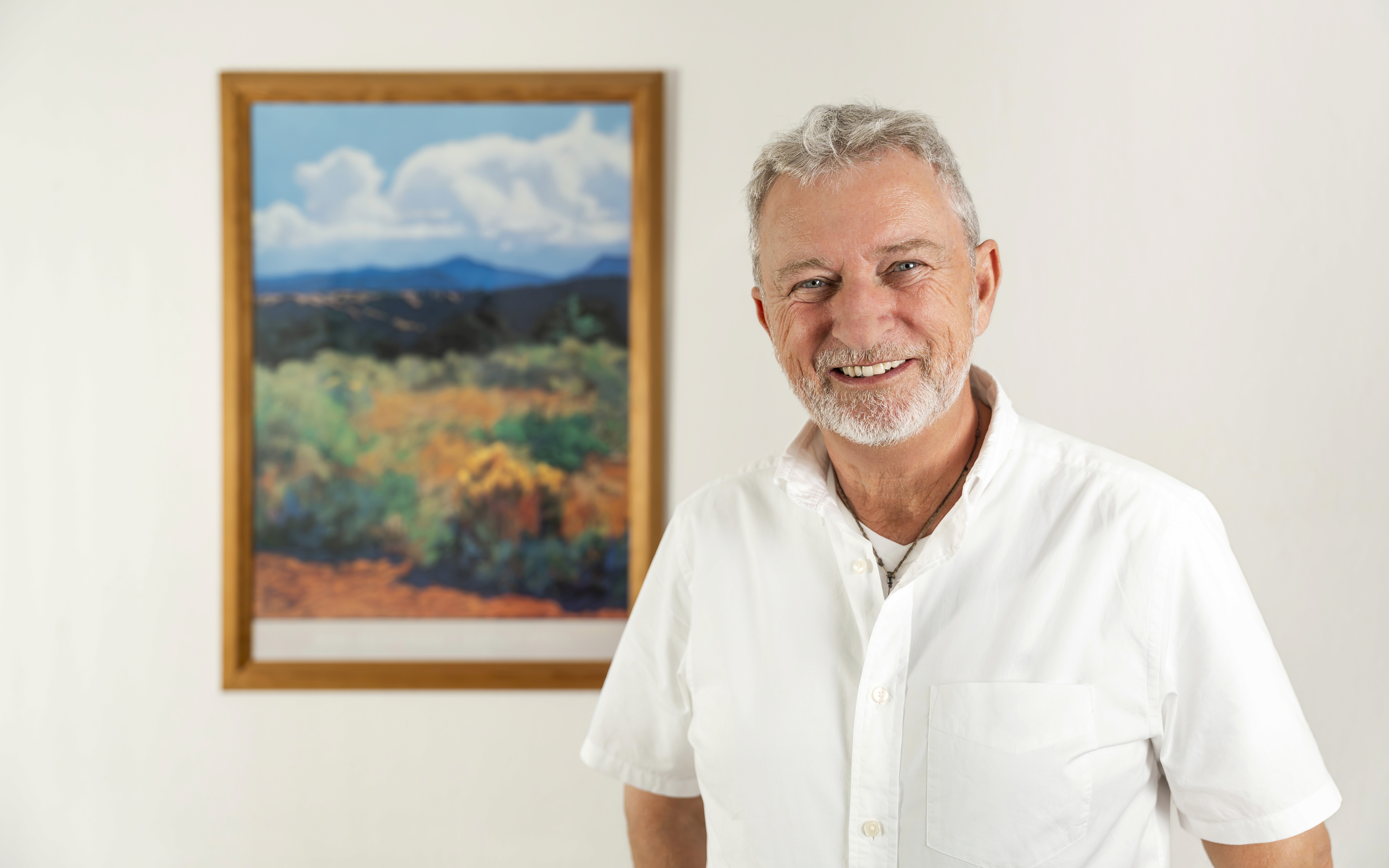 Smiling man with glasses and a short beard wearing a white t-shirt stands against a deep purple background, conveying a cheerful and friendly tone.