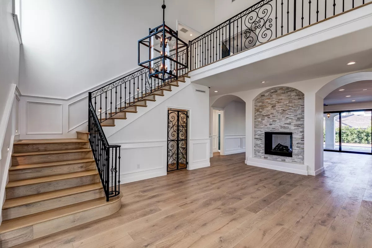 Grand entryway remodeling featuring a wooden staircase, ornate black railing, stone fireplace, and large windows overlooking a garden.