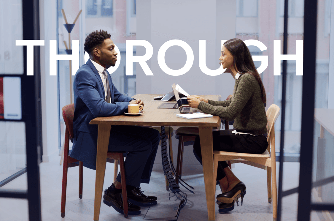 Two people, a man and a woman, sitting at a table and having a conversation in an office setting. The word "THROUGH" is prominently displayed in the background.