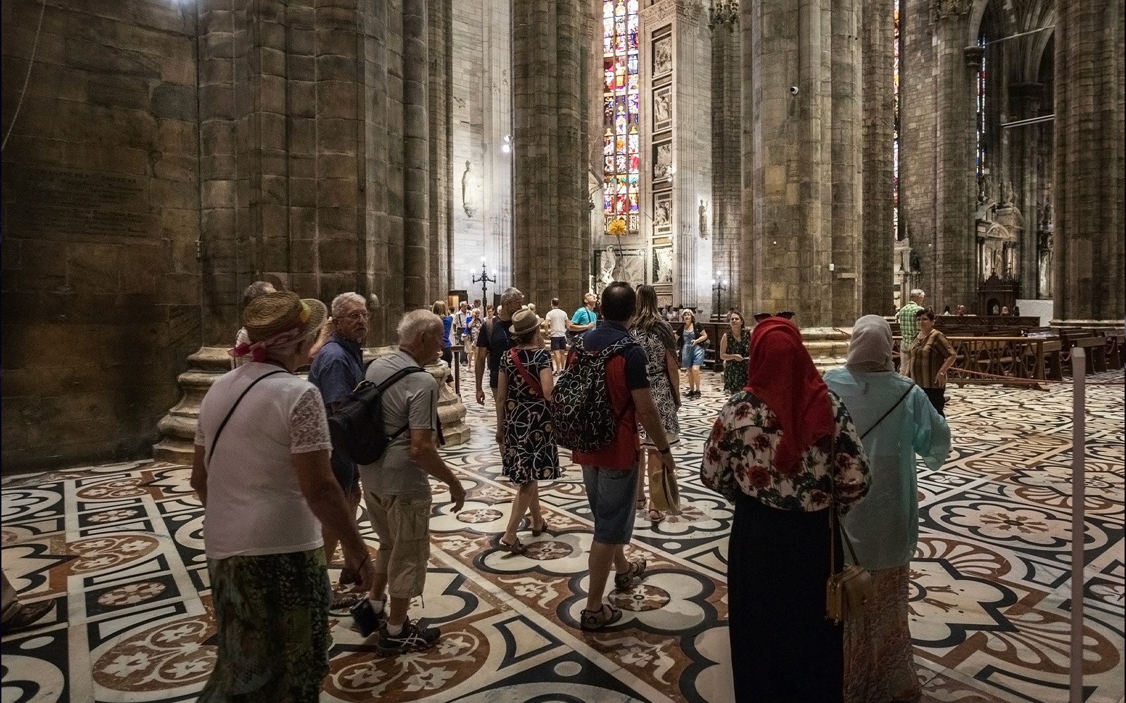 Du khách bên trong nhà thờ Duomo di Milano đang chiêm ngưỡng các cửa sổ kính màu và kiến trúc.