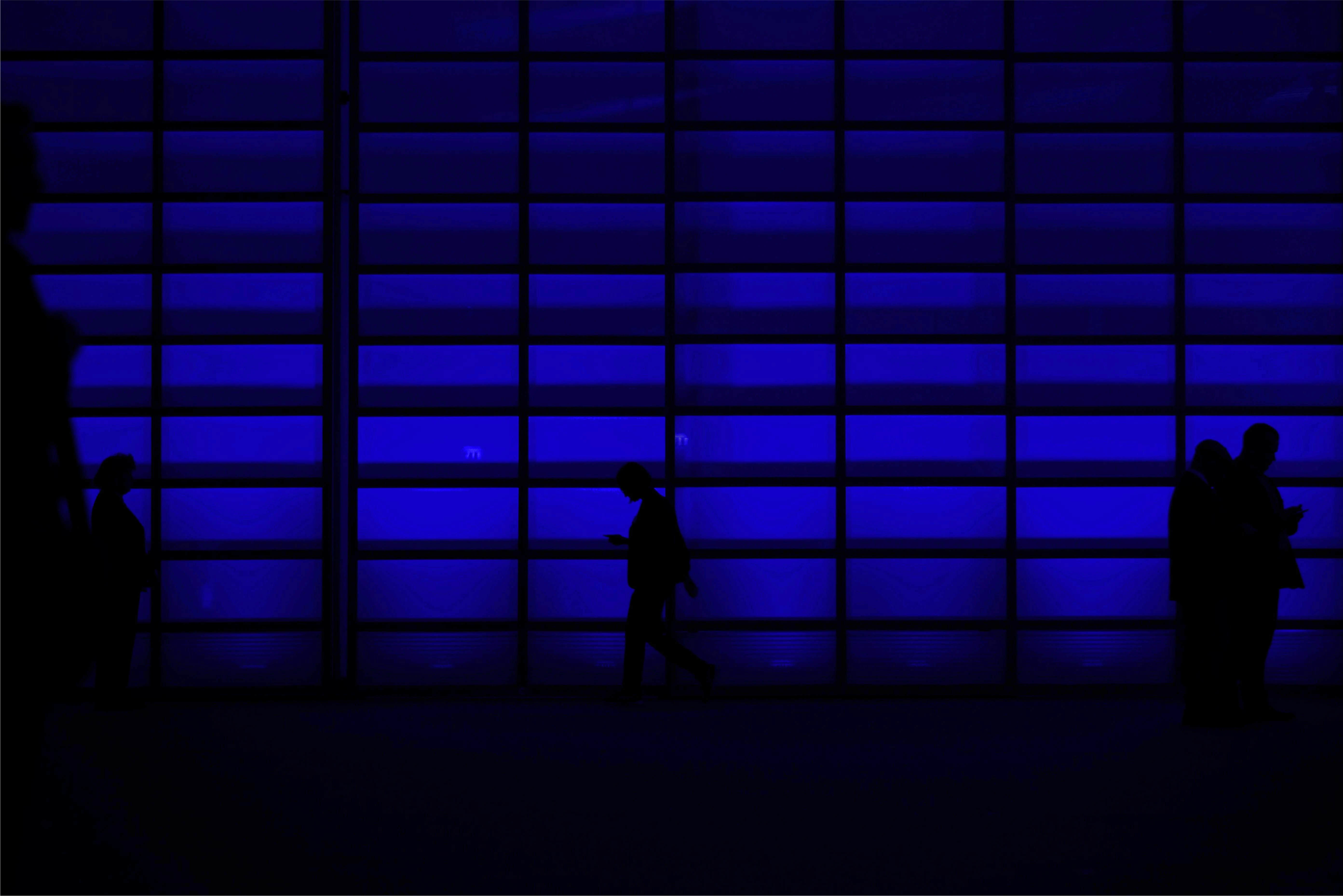 Silhouettes of people against a backdrop of blue lights and a grid pattern, creating a vibrant, atmospheric scene.