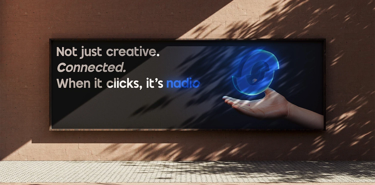 Hand holding blue globe on advertisement board with text Not just creative. Connected. When it clicks.