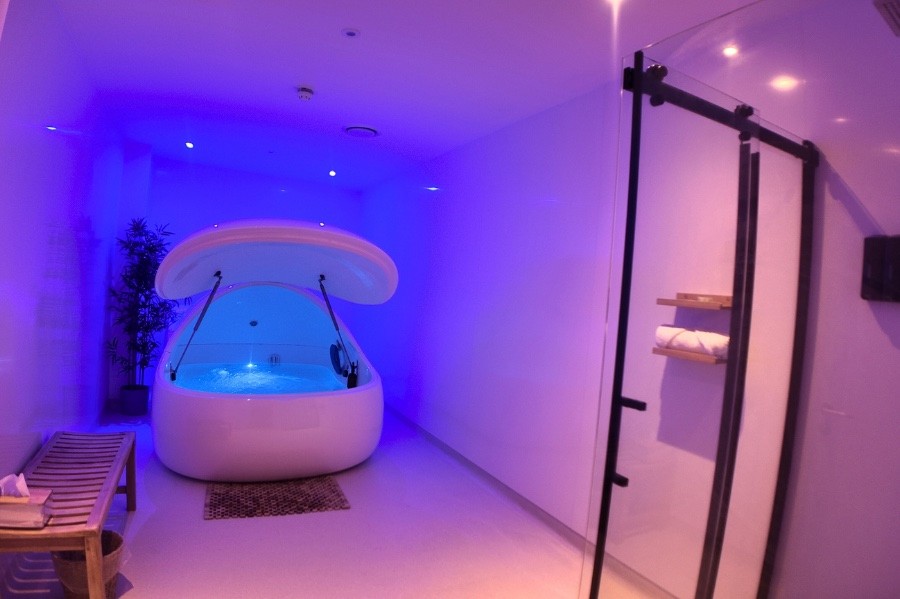 Private float room at Floatworks Angel with an open Float Pod lit in blue and purple, a wooden bench and a glass shower
