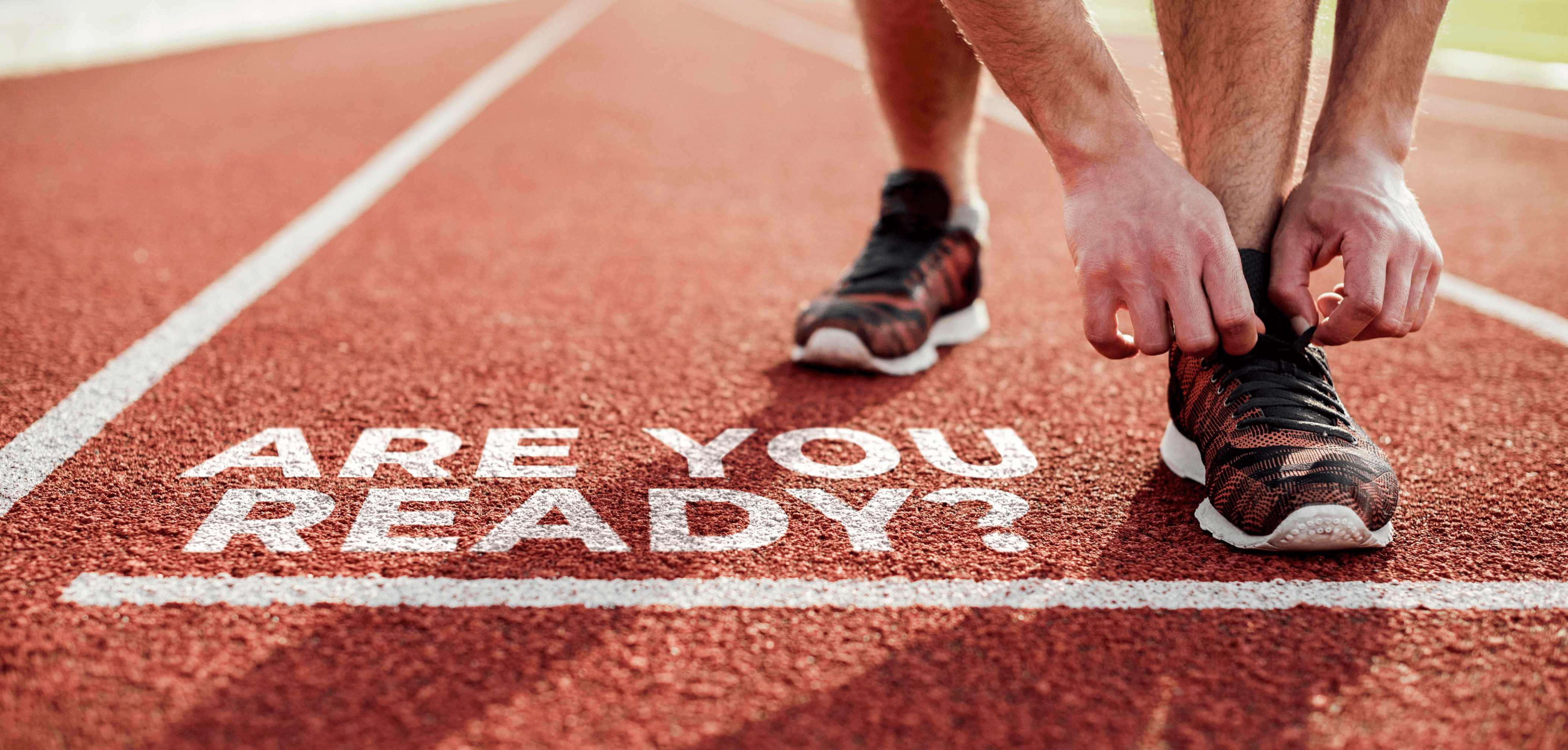 Runner tying their shoe at the starting line of a track, beside the words “Are you ready?”