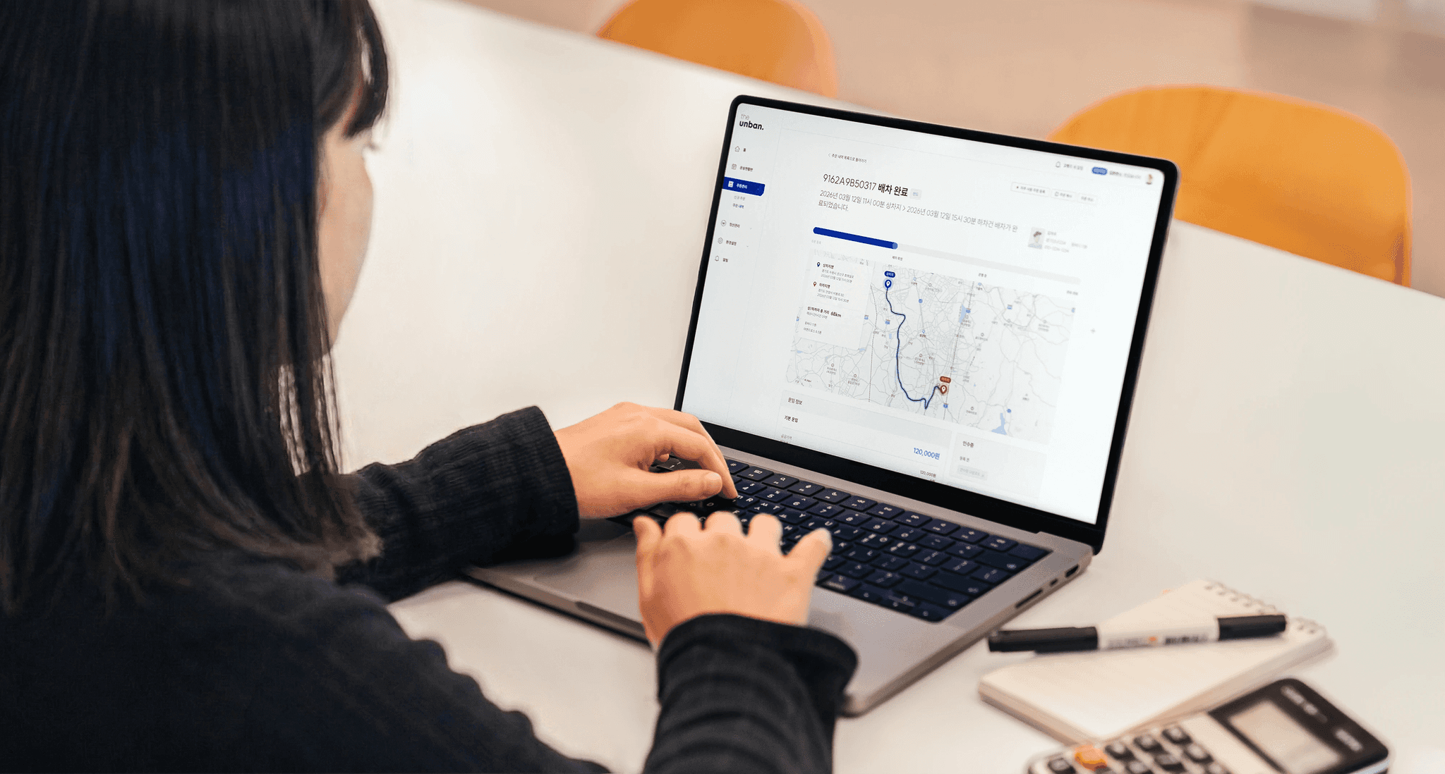 CJ대한통운 더 운반 바로주문 서비스를 소개하는 히어로 이미지로, 노트북 화면에 배차 완료 상태의 운송 경로 지도와 운임 정보가 표시되어 있습니다. AI가 산출하는 최적 운임으로 전국 차주 매칭과 실시간 관제까지 한 번에 처리할 수 있음을 안내합니다.