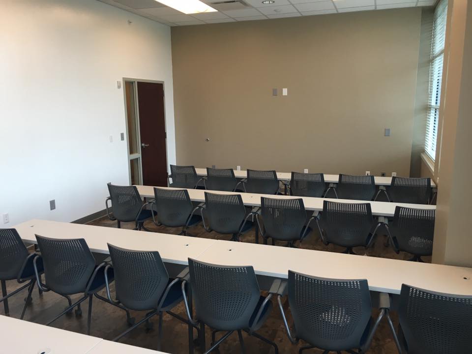 A meeting room with rows of black chairs facing a blank wall and a door, designed for gatherings or presentations.