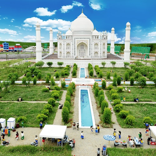 Miniature Taj Mahal replica with gardens and reflective pools. Figures of people are scattered throughout the park, creating a lively scene.