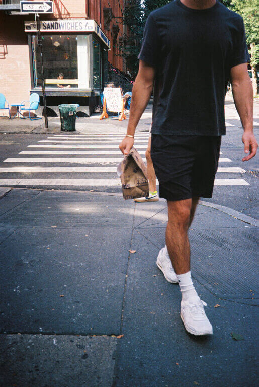 A man walking on the sidewalk holding a bag of bagels from Edith's 