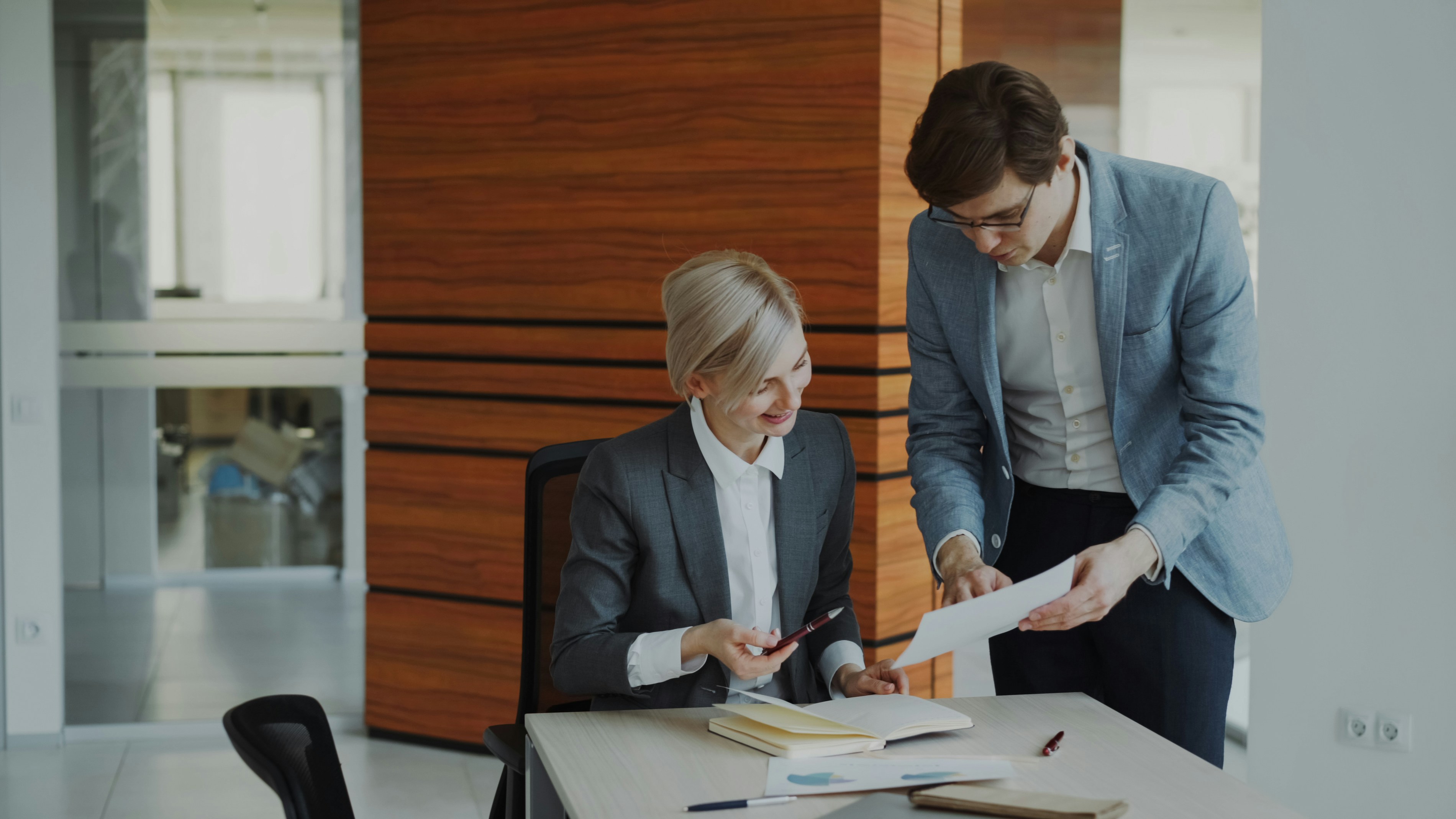 Two professionals reviewing a document together at an office desk with notes and charts.