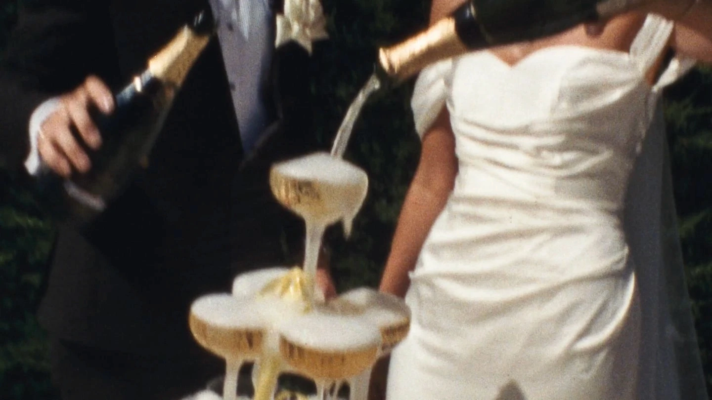 A bride and groom pour champagne into a cascading tower of glasses, with frothy bubbles overflowing, symbolizing celebration and elegance at a wedding reception.