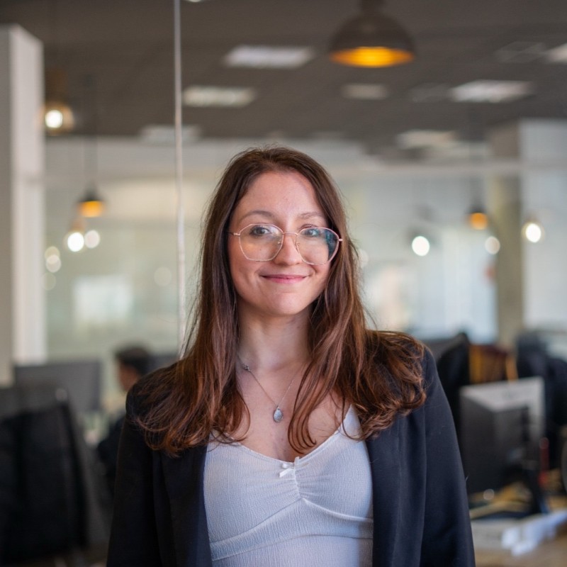 Donna sorridente con occhiali e blazer in un ambiente d’ufficio