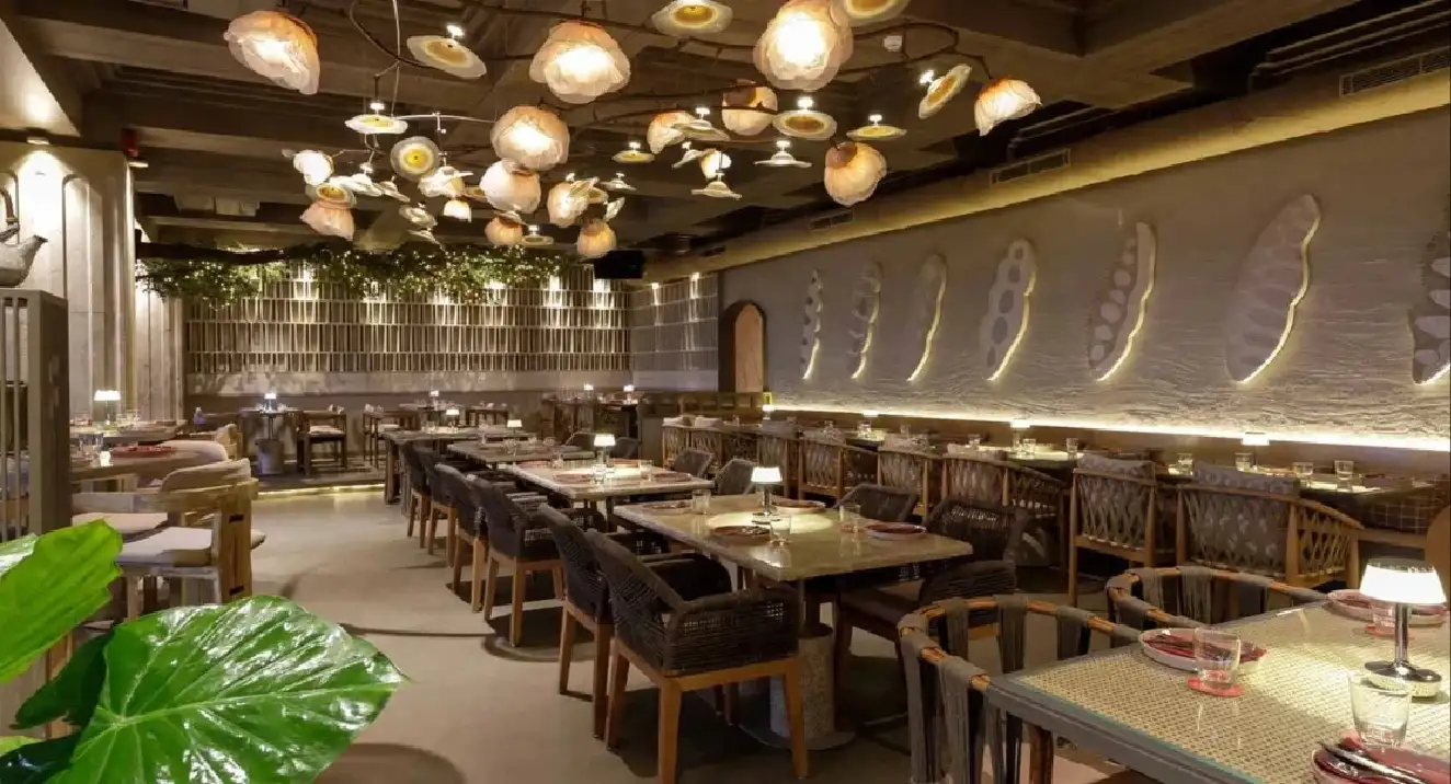 A luxurious indoor pool area with a panoramic view of a city at sunset. Comfortable lounge beds with soft fabrics surround the pool, while warm ambient lighting enhances the sophisticated atmosphere. The space combines modern elegance with a tranquil vibe.