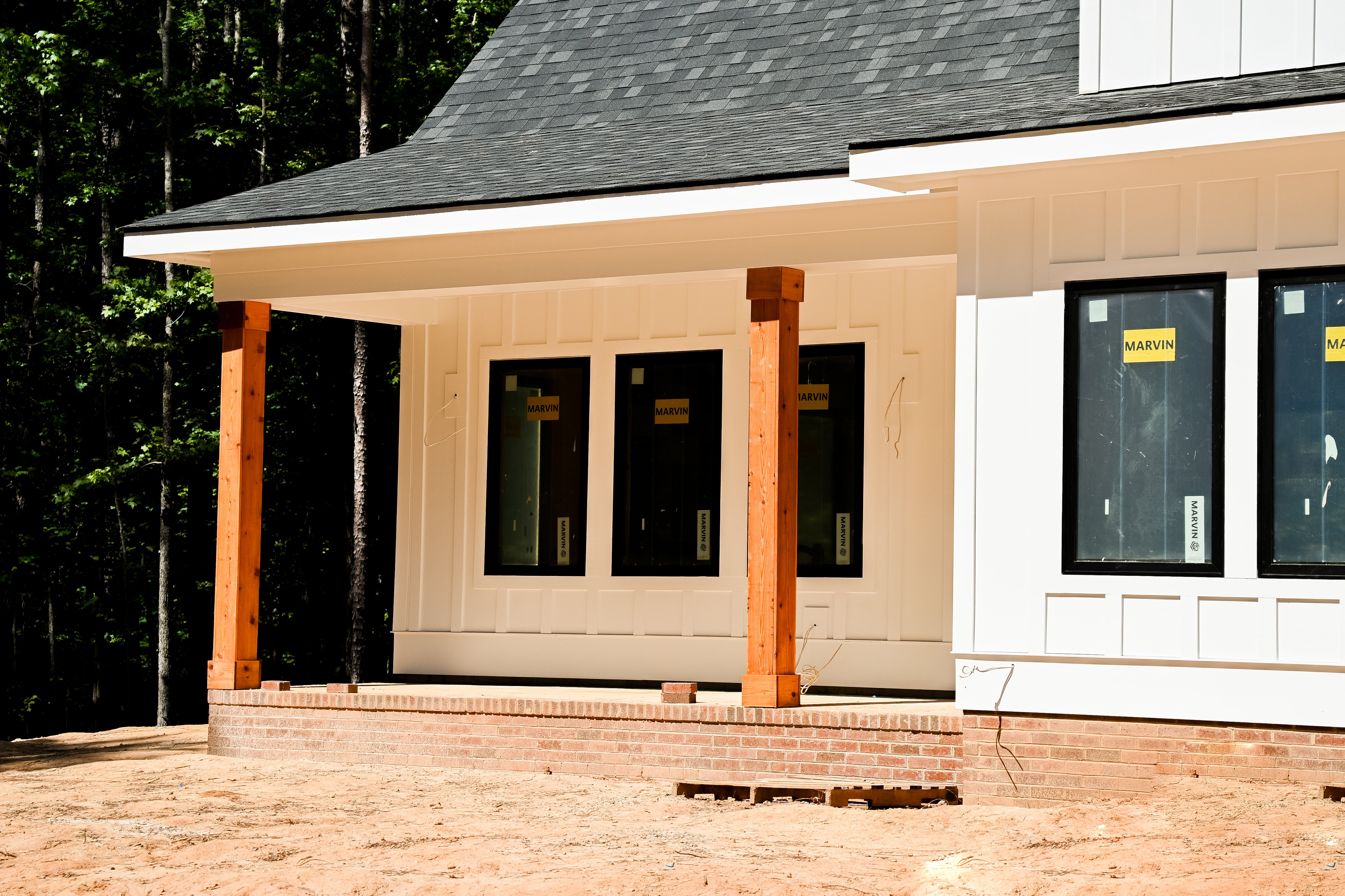 Pórtico frontal techado con columnas de postes de cedro teñido y cimientos de ladrillo en una casa personalizada bajo construcción en Carolina del Norte