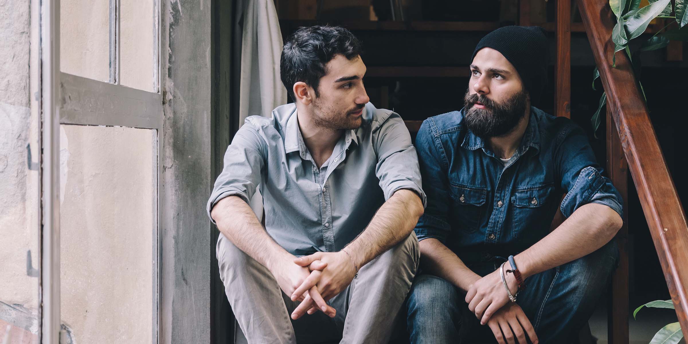 Two men, one with a beard and beanie hat sat on an indoor staircase