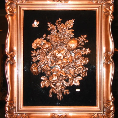 Khung gỗ chạm khắc tinh xảo với hoa văn màu đồng và một con bướm nhỏ trên nền đen.