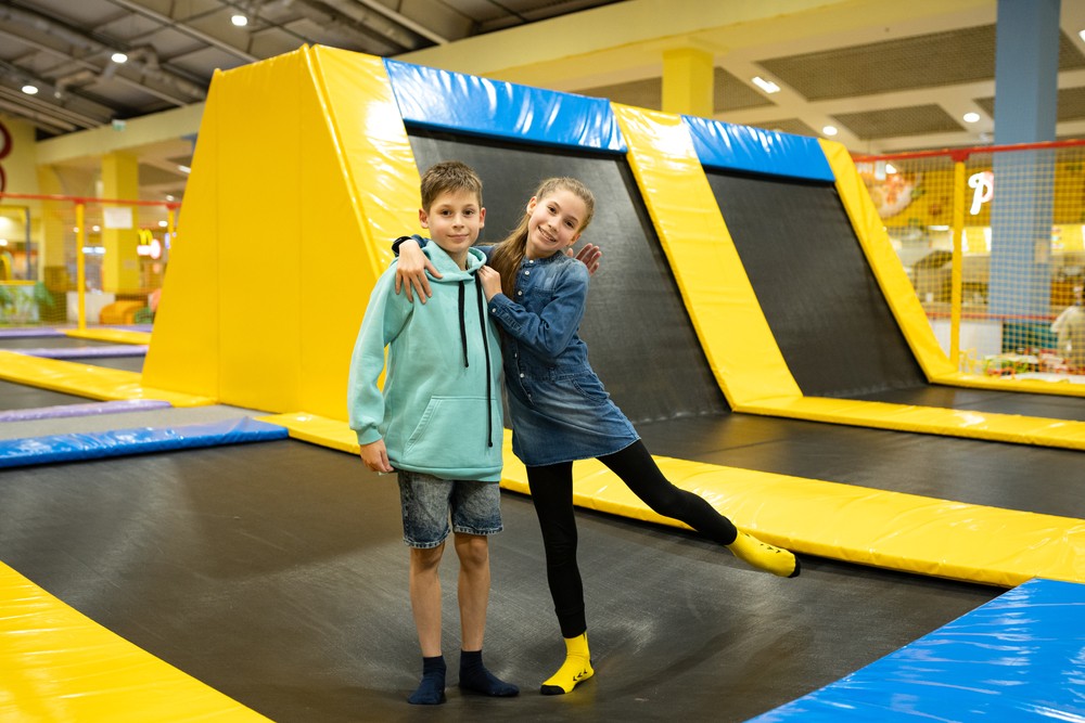A young person with curly hair smiles at the camera while sitting in front of a laptop against a dark background.