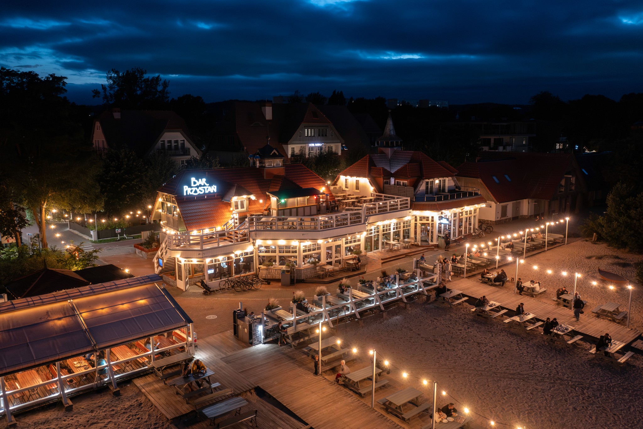 Widok z lotu ptaka na restaurację przy plaży z lampkami i tarasem o zmierzchu.