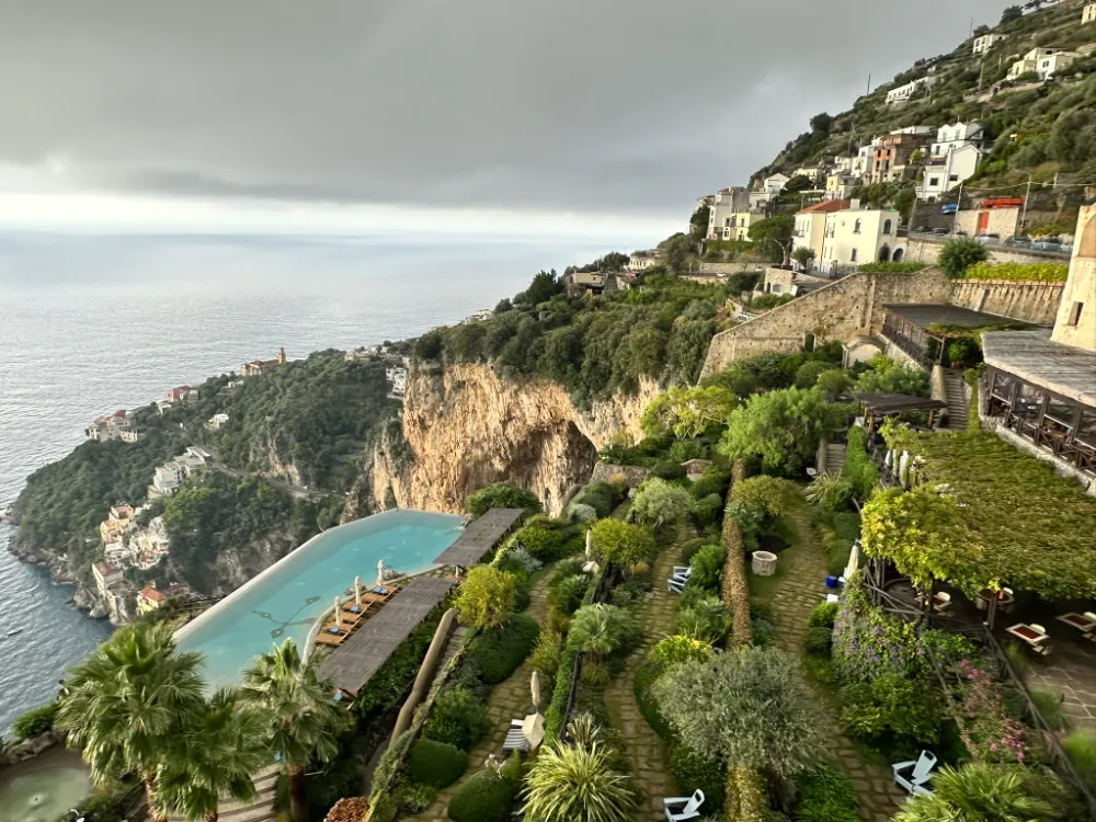 The terraced gardens and infinity pool at Monastero Santa Rosa seen from above, with the coastline beyond.