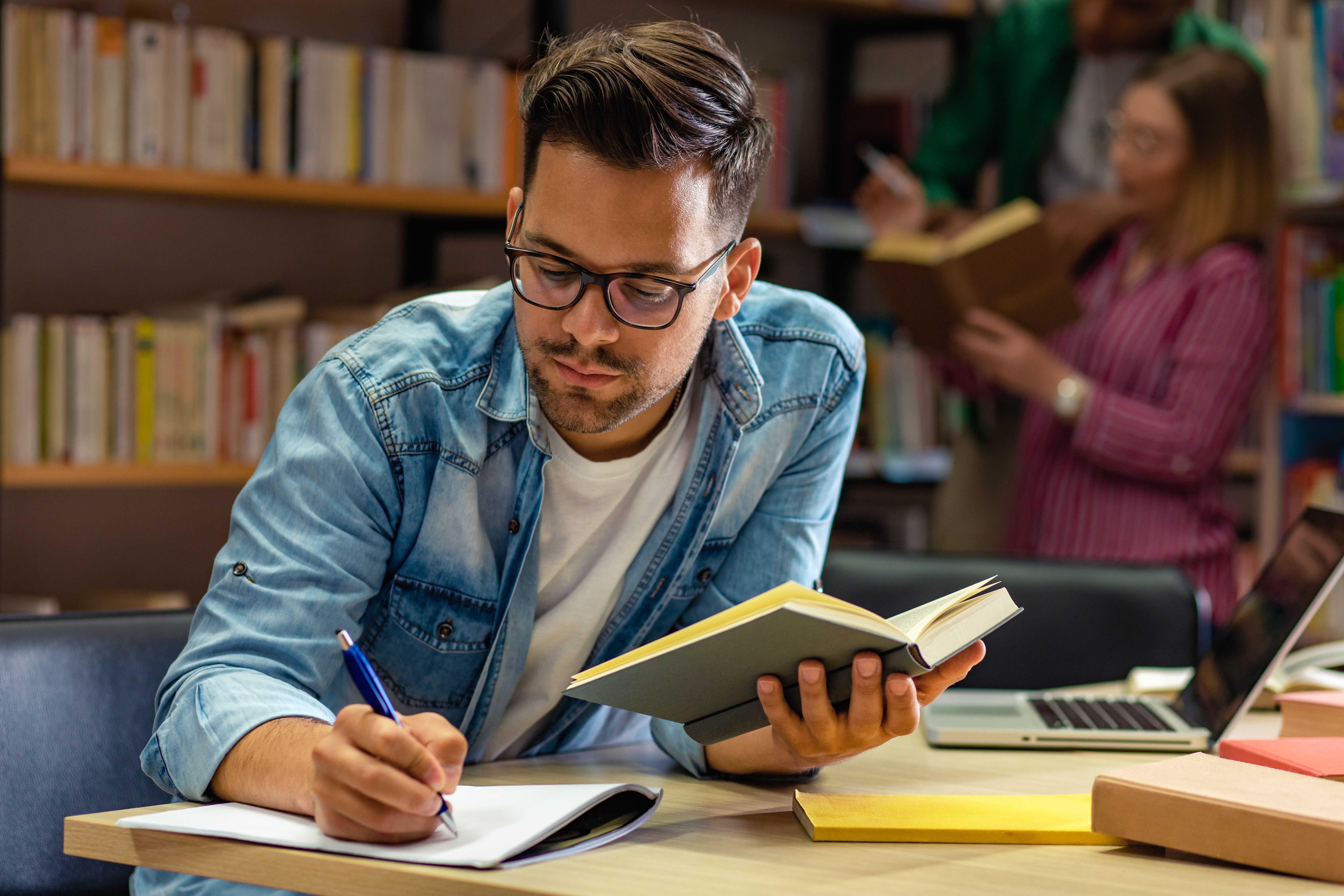 Student taking notes and reading at a desk in a library at LBS