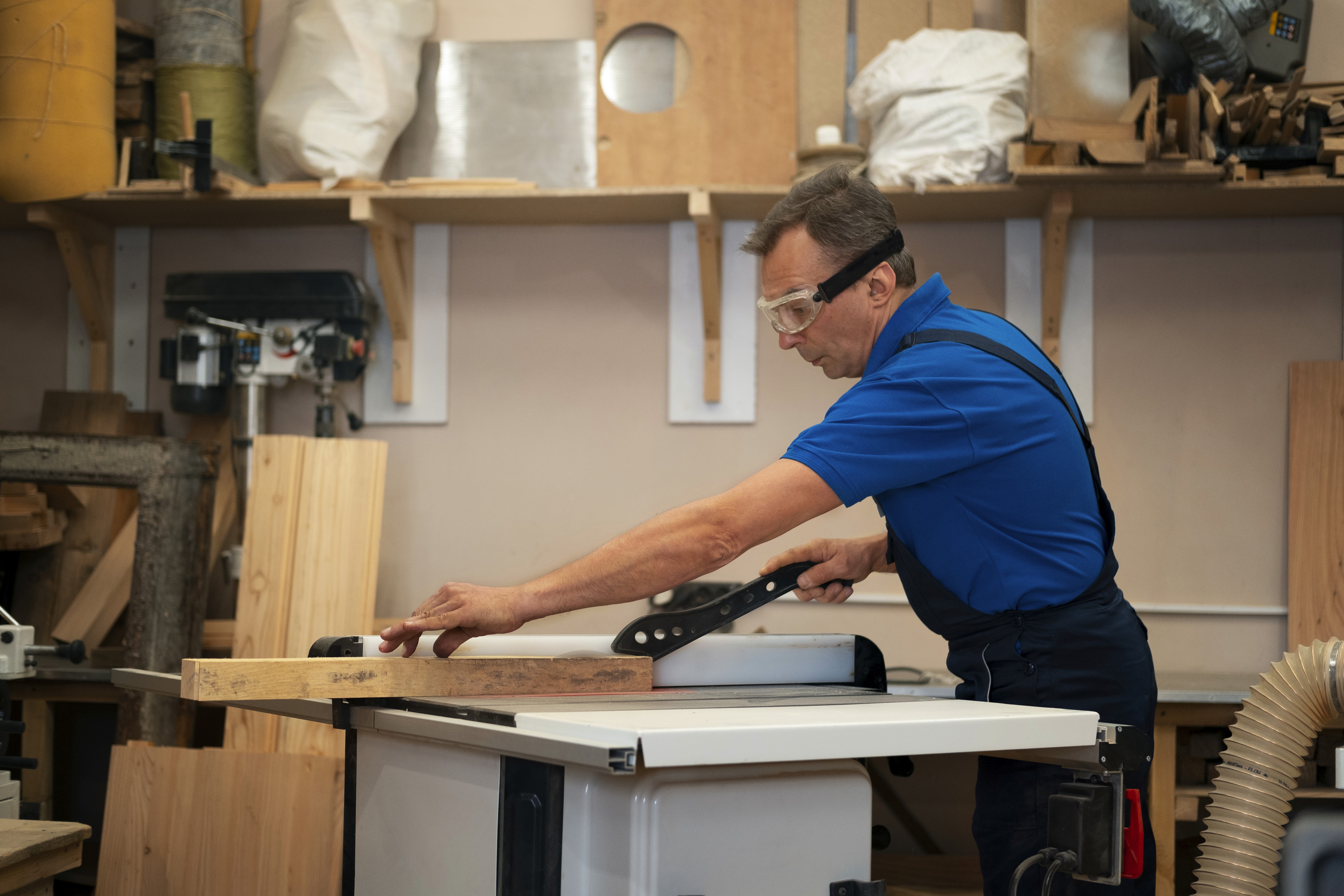 Man assembling a white table with brown legs. The man is wearing a blue jumpsuit and leaning over the furniture.