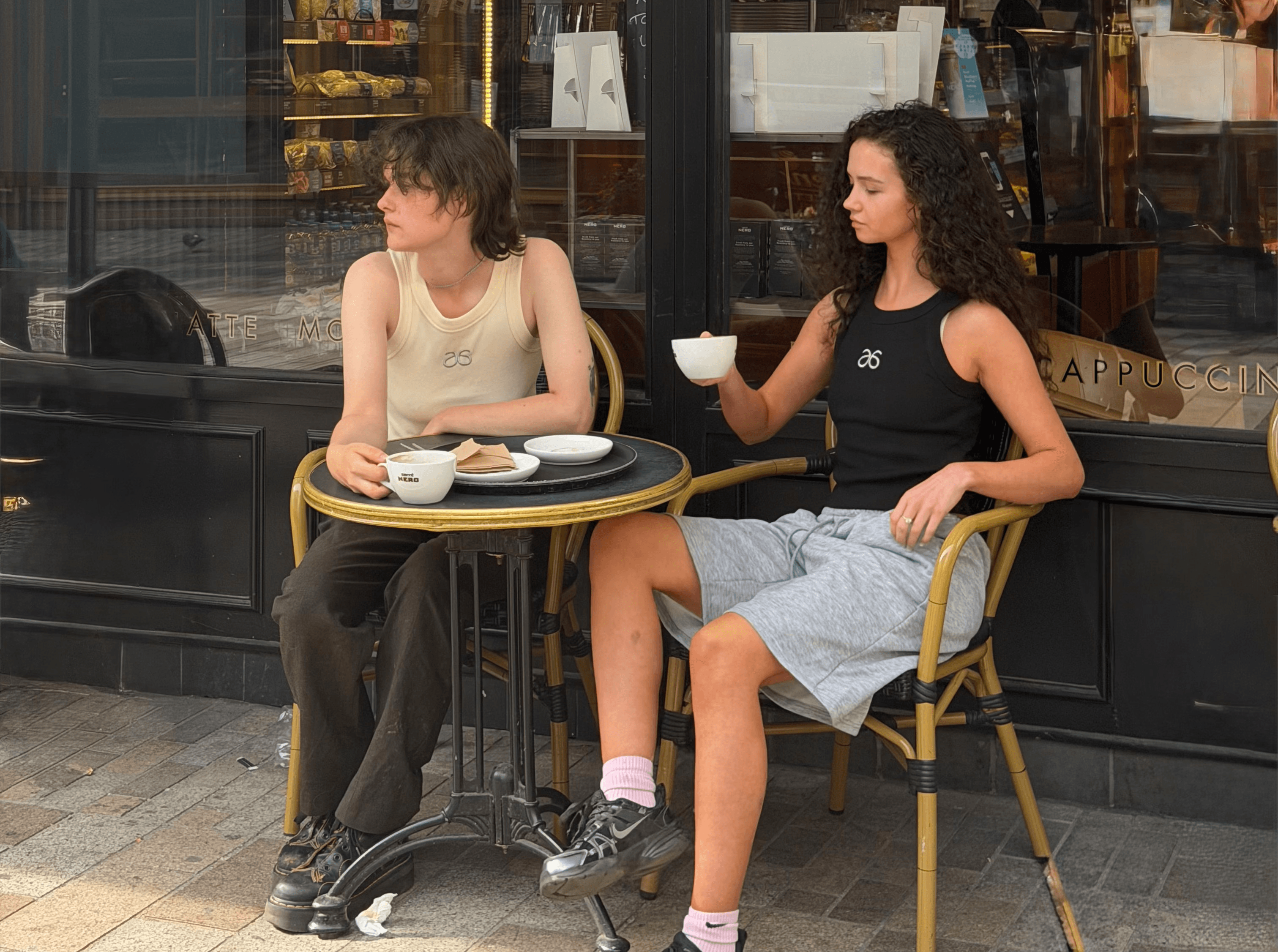 Two women wearing 6ISTY6 clothing and enjoying coffee together at a café