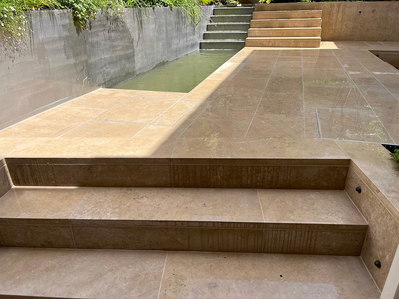 A view of outdoor steps leading up to a paved area, surrounded by green foliage and stone walls.