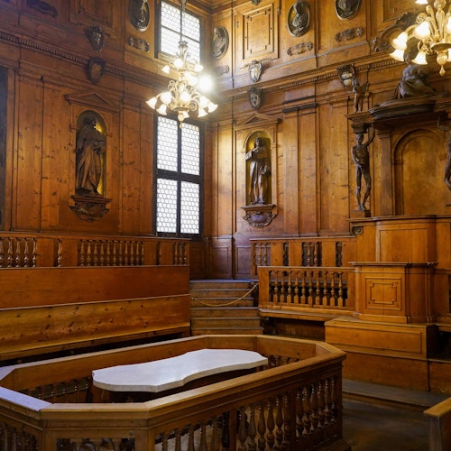 חדר עם חיפוי עץ על הקירות, פסלים על הקירות, נברשות, פודיום מרכזי עם משטח שיש, ומקומות ישיבה מעוצים במדרגות.