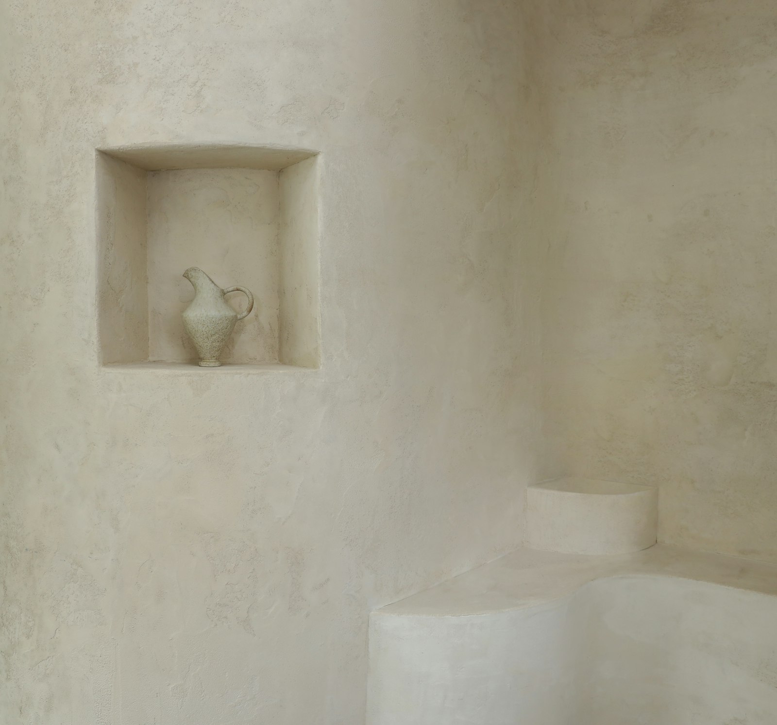 Lime-plastered wall with a small niche holding a ceramic jug