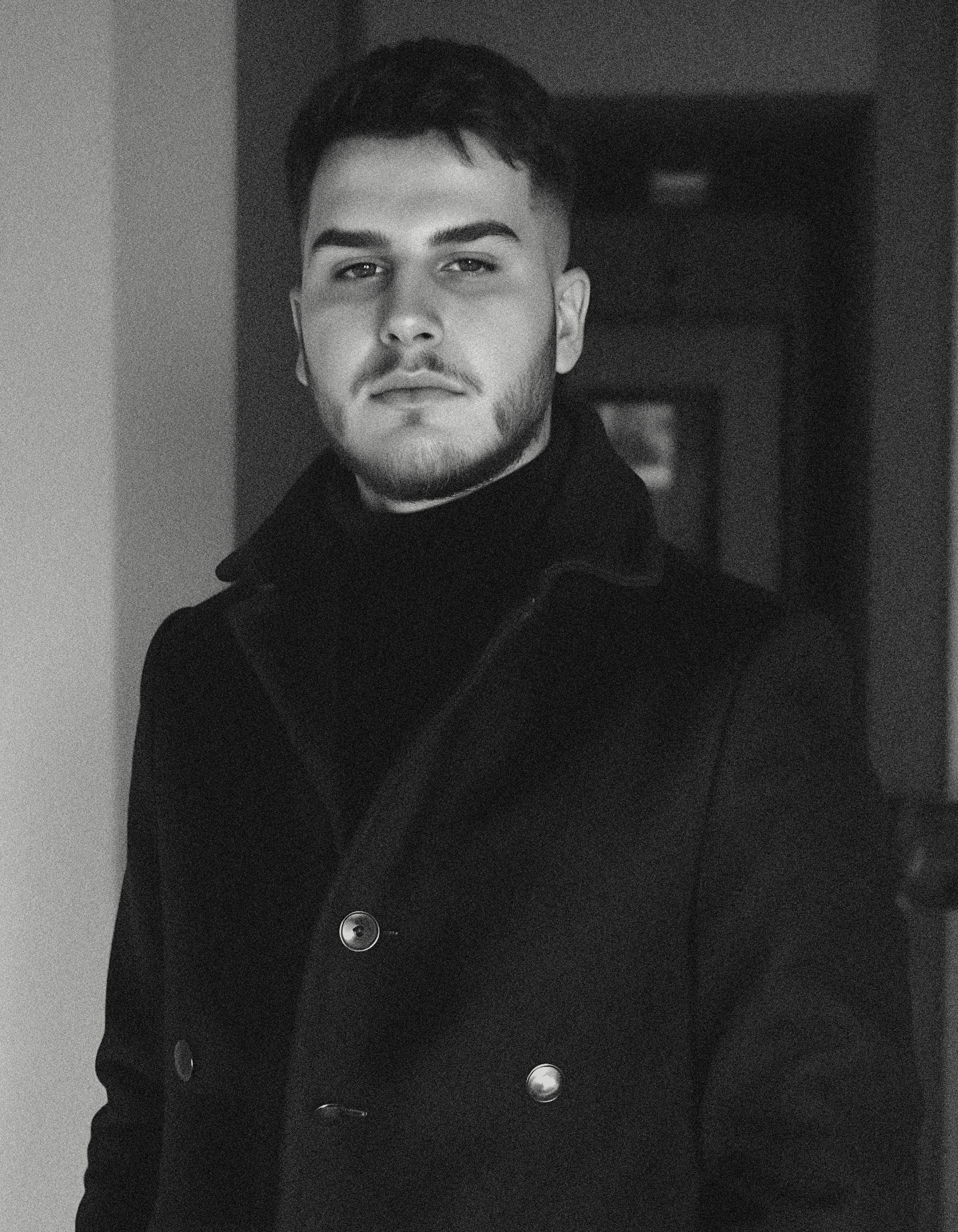 Person wearing a blue puffer jacket and red backpack standing in front of a light blue building on a city street.