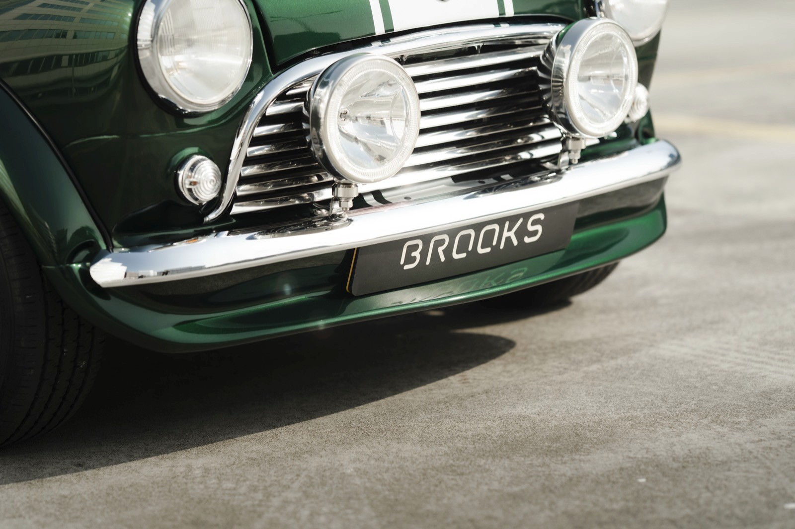 Front detail of a vintage green car, showcasing chrome accents and a classic design on a concrete surface.