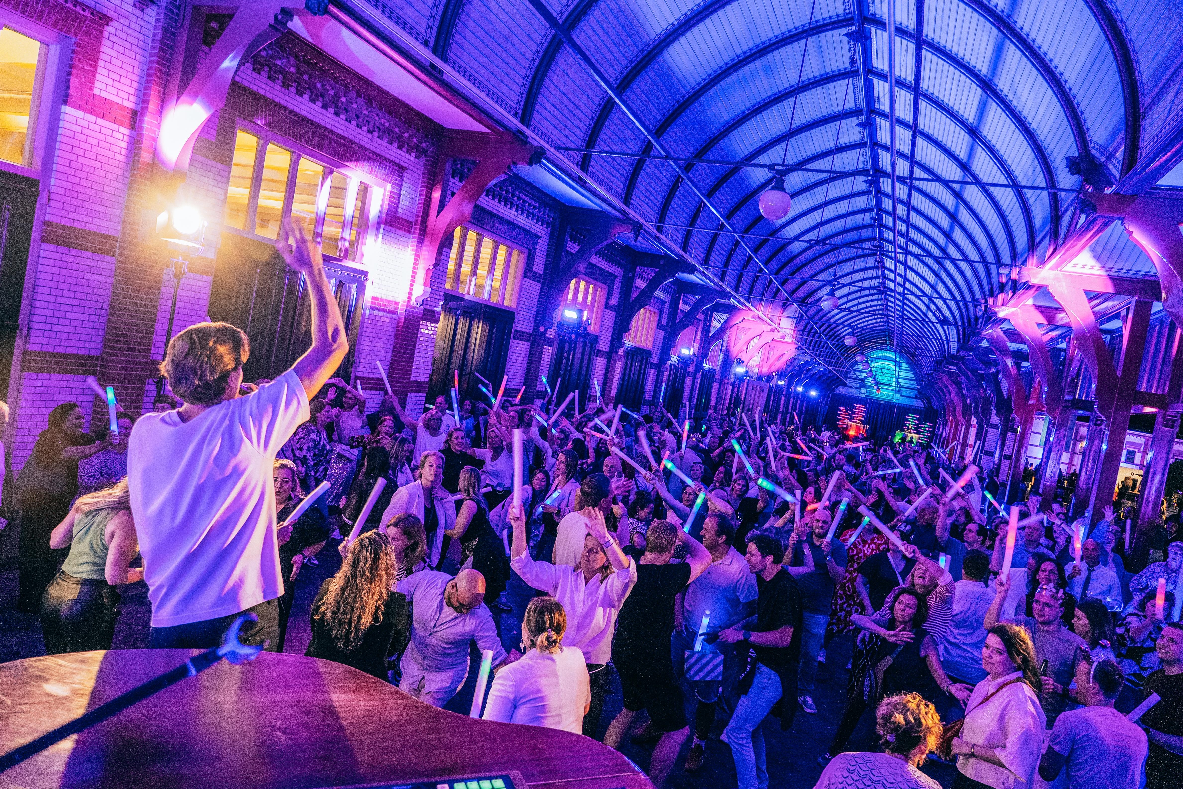 Lars van DJ Zingt Live draait achter de booth voor een dansend publiek met glow sticks tijdens een groot feest.